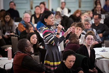 Woman in a crowded room stands facing left, holding a microphone