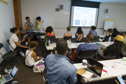 Group of individuals sitting at table watching a presentation