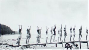Many young women standing on a dock at the beach with their hands stretched toward the sky.