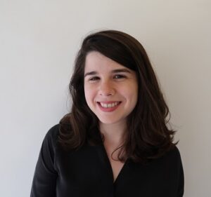 A woman with dark brown hair, wearing a black shirt, smiling at the camera