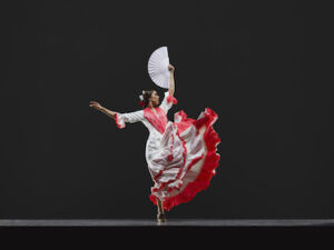 A dancer in red and white with a white fan in hand, arms outstretched, and skirts flying