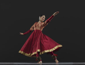 A dancer in red and gold smiles with arms outstretched