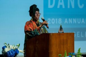 A woman with a black head-wrap speaking at a podium