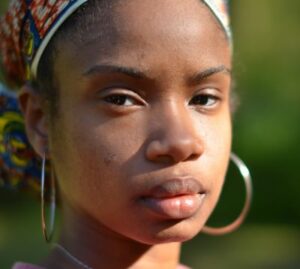 A woman with a scarf on her head and hoop earrings looks directly at the camera