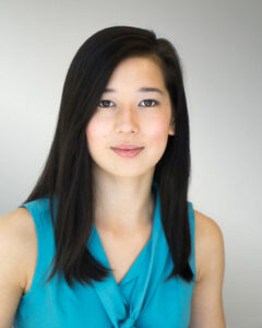 A Japanese-American woman with long, dark hair and a bright blue shirt smiling. 