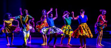 Eight dancers in colorful costumes on stage