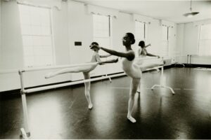 Three dancers stand at a barre in arabesque.