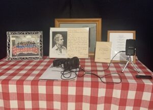 Photos and recording equipment sit on a table with a red checked cloth.