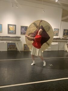 A woman in a red shirt dances, holding a large disc of cloth.