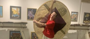 A woman in a red shirt dances holding a disc of fabric