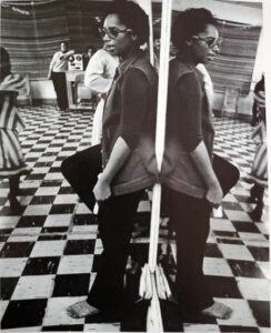 A woman standing against a mirror in a dance studio with a checkerboard floor.