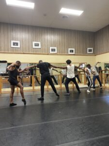 A line of dancers holding hands in a dance studio.