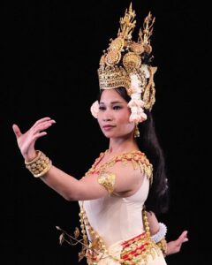 A Cambodian dancer wearing a costume and gold headdress, framed from the waist up.