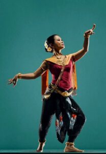 Full-body shot of a Cambodian dancer against an aquamarine background.