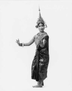 A cambodian woman in a large headdress and elaborate formal wear standing in a dance pose.