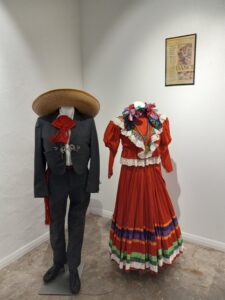 A black suit and a red dress on display with a framed poster behind them.
