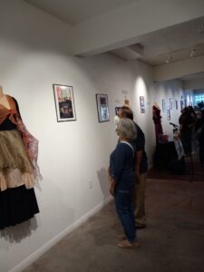 Two people looking at a poster hanging at a wall. Costumes hang on the wall nearby.
