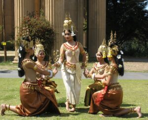 One dancer standing and four dancers kneeling in a circle around her, all wearing elaborate traditional Cambodian garb.