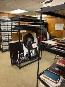Shelves, boxes, and framed photographs in an archive room.