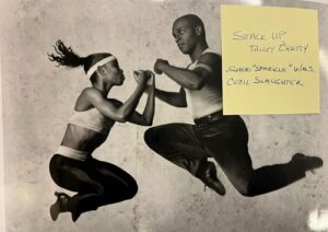 A black and white photo of two dancers jumping in the air.