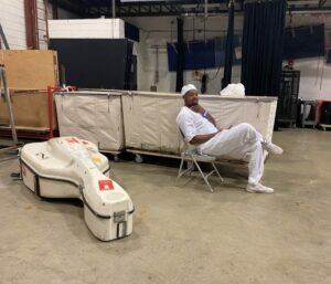 A person dressed in white with a large, white instrument case on the round next to them.