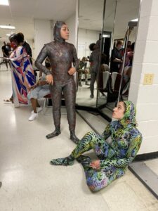 Two dancers in body suits. One stands and one sits.