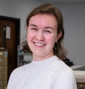 A white woman with short brown hair, wearing a white sweater, smiling.