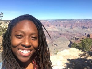 A Black woman smiles at the camera, with a canyon in the background