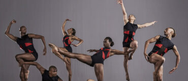 A group of seven dancers in red and black in various poses