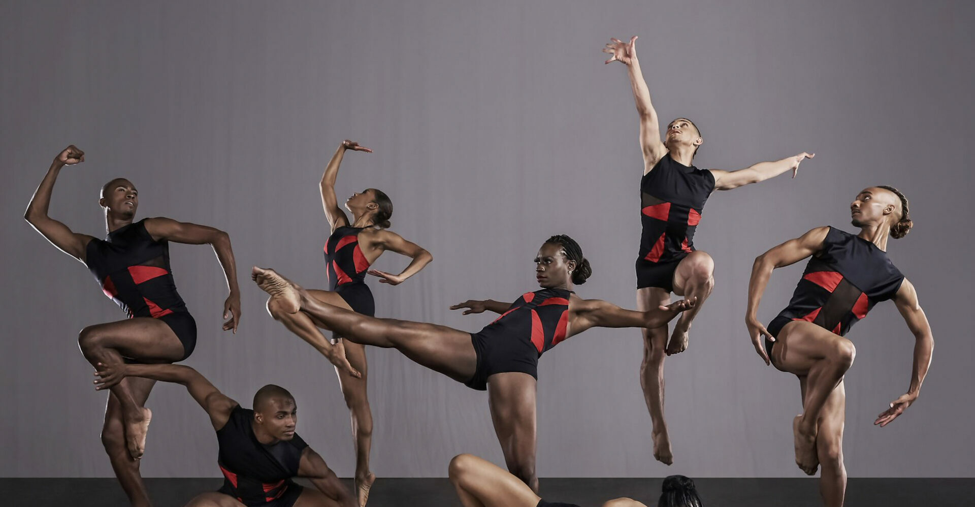 A group of seven dancers in red and black in various poses