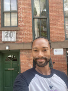 A selfie of Abdiel in front of a brick building that says "2Q"