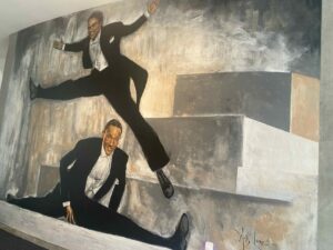 A painting of two dancers in the splits and leaping