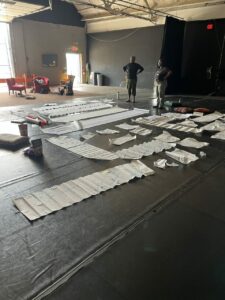 Two people standing in a large room with large rolls of paper at their feet.