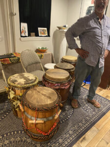 five drums with colorful adornments. Next to them a man stands with his hands on his hips. 