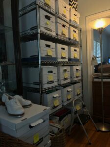 A tall shelf with five rows of three files boxes each and a pair of tap shoes.