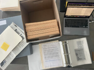 An arial view of a box with folders in it, an open binder with papers in it, and a laptop open on a desk.
