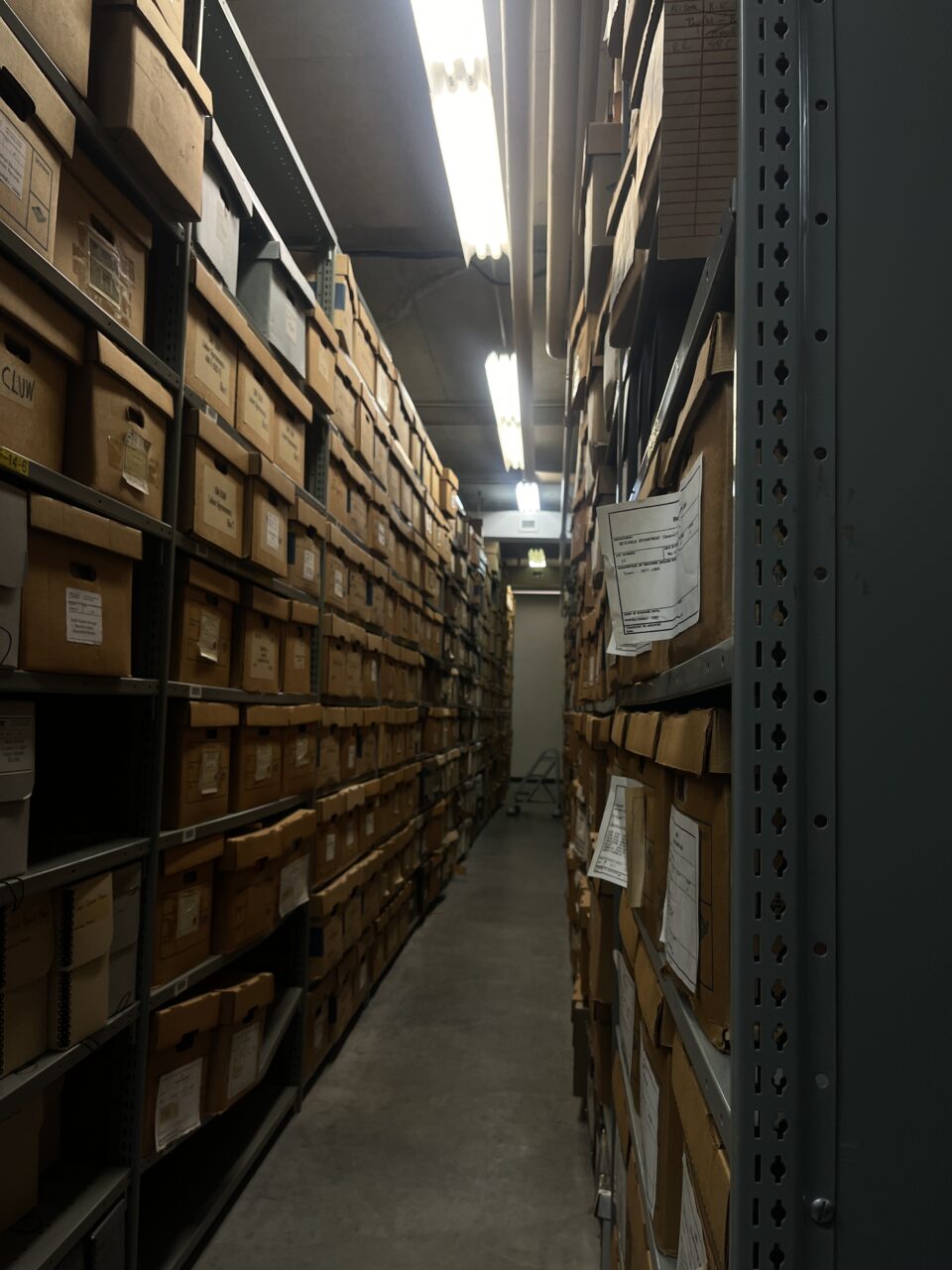 A long hallway with tall shelves lining it covered in brown bankers boxes.