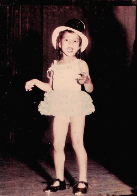Sepia toned, vintage image of a young child with a top hat, leotard and tutu, and tap shoes on.